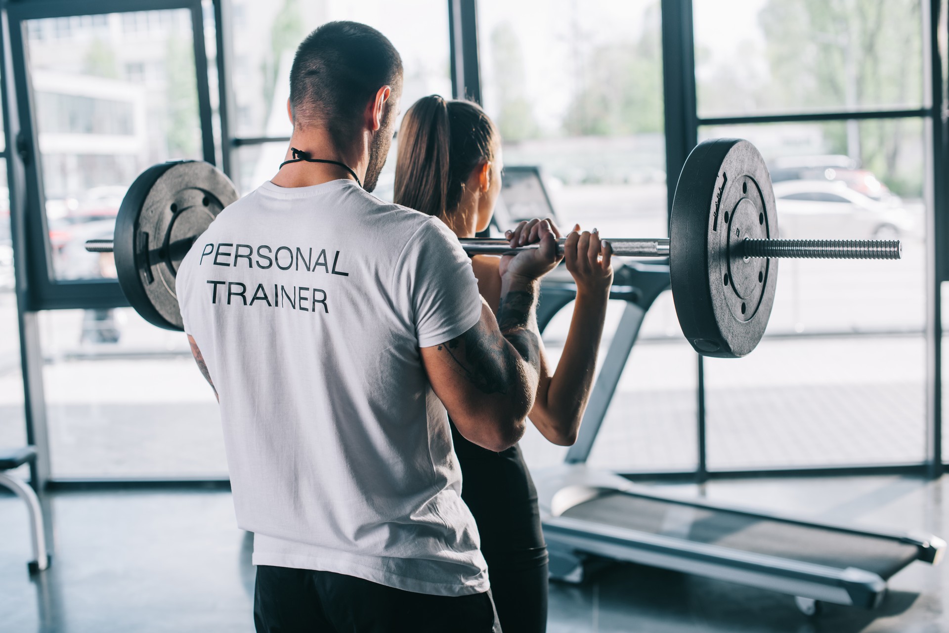 male personal trainer helping sportswoman to do exercises with barbell at gym